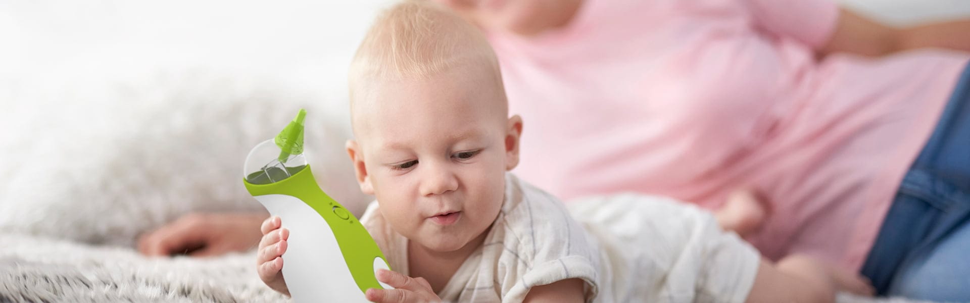 Una donna e un bambino sdraiati sul tappeto tenendo l'aspiratore nasale portabile Nosiboo Go