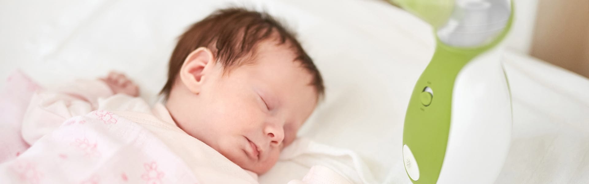 Un bebè dorme tranquillamente nel lettino accanto all'aspiratore nasale portabile Nosiboo Go