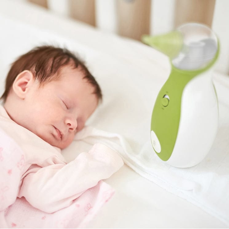 Un bebè dorme tranquillamente nel lettino accanto all'aspiratore nasale portabile Nosiboo Go
