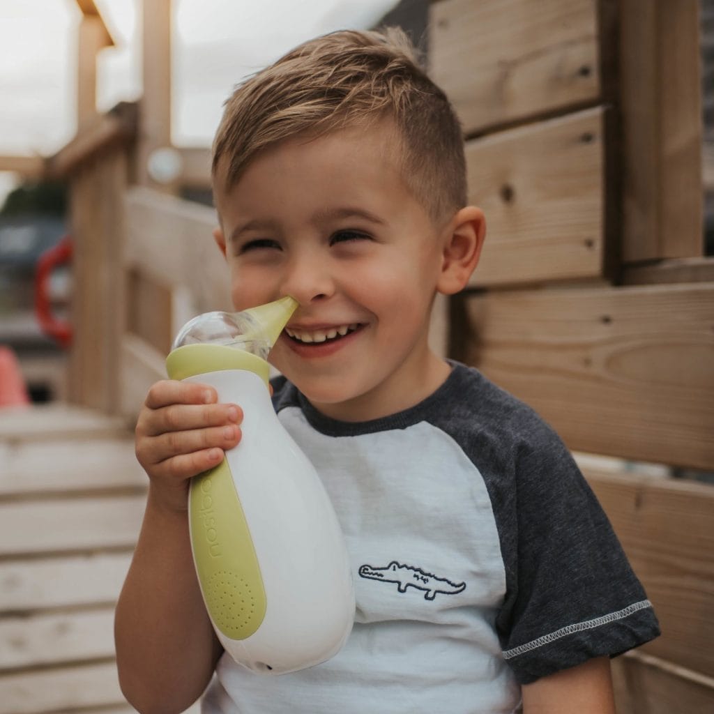 Bambino sorridente con un aspiratore nasale elettrico portatile Nosiboo Go in mano