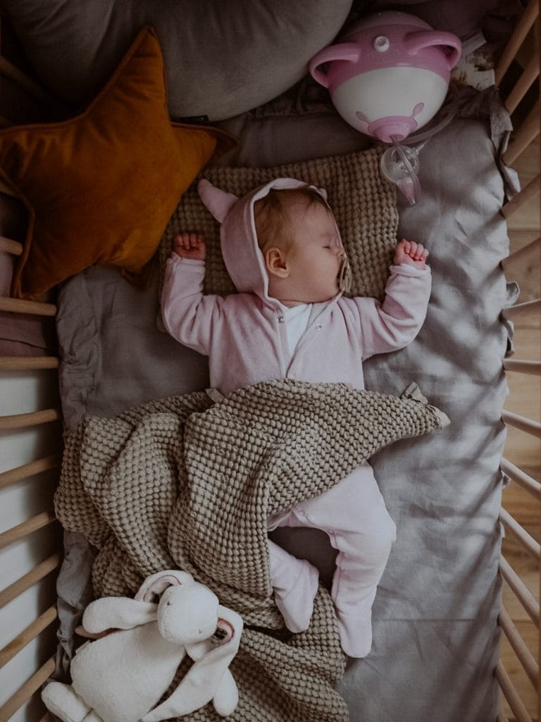 Una bambina dorme in una culla in vimini accanto all'aspiratore nasale elettrico Nosiboo Pro