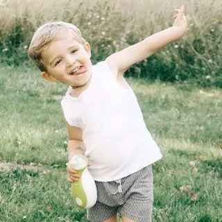 Un bambino felice tiene l'aspiratore nasale portatile Nosiboo Go, e gioca fuori nel parco