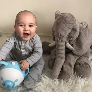 Un bambino affascinato tiene un Nosiboo Pro a forme di un orsetto seduto sul letto accanto a un elefante di peluche