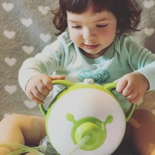 Una bambina chi tiene sorridendo l'aspiratore nasale elettrico Nosiboo Pro a forma di un orsetto per le orecchie