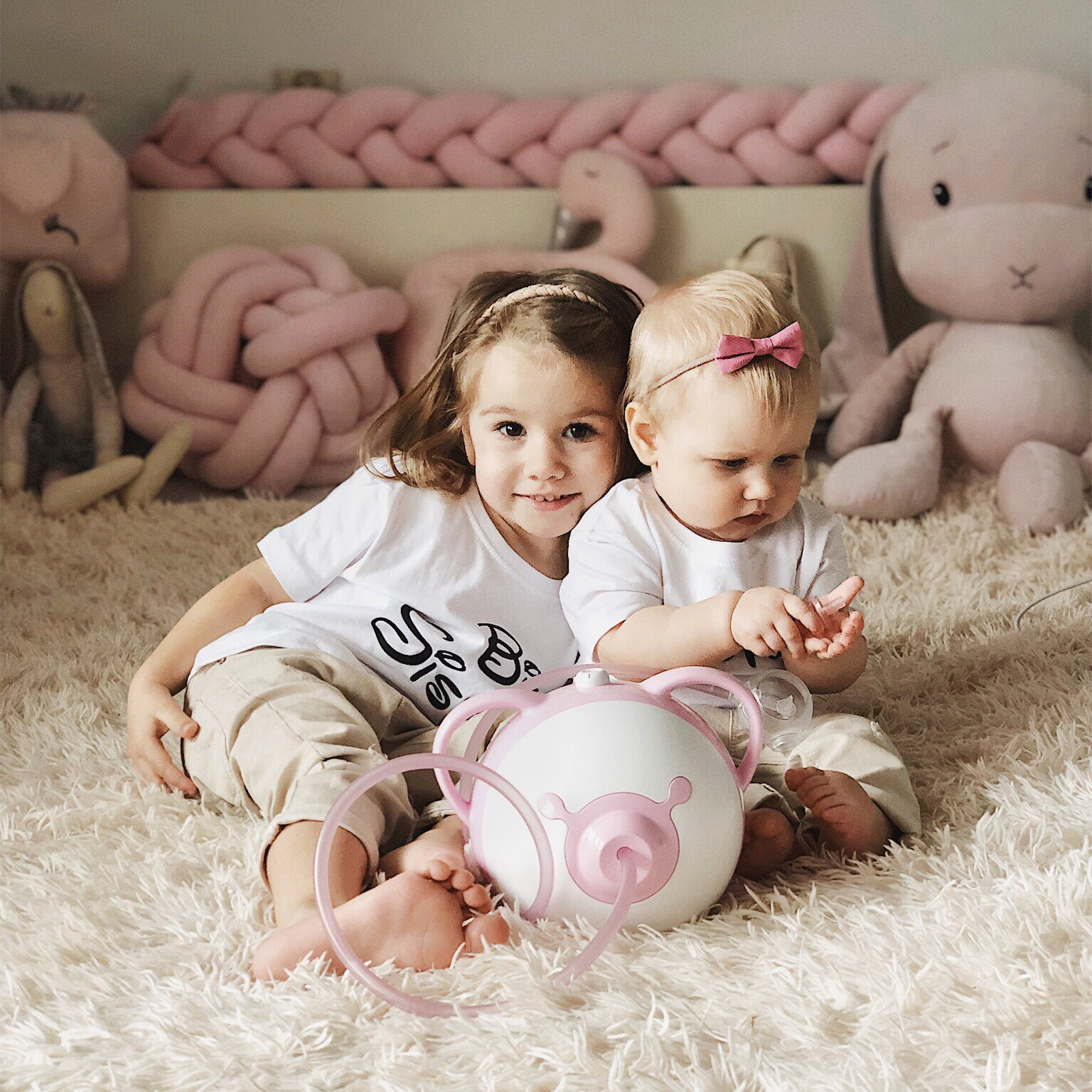 Due bambine carine siedono assieme sul letto accanto all'aspiratore nasale elettrico Nosiboo Pro