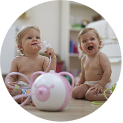 Due bambine felici siedono sul pavimento con l'aspiratore nasale elettrico Nosiboo Pro