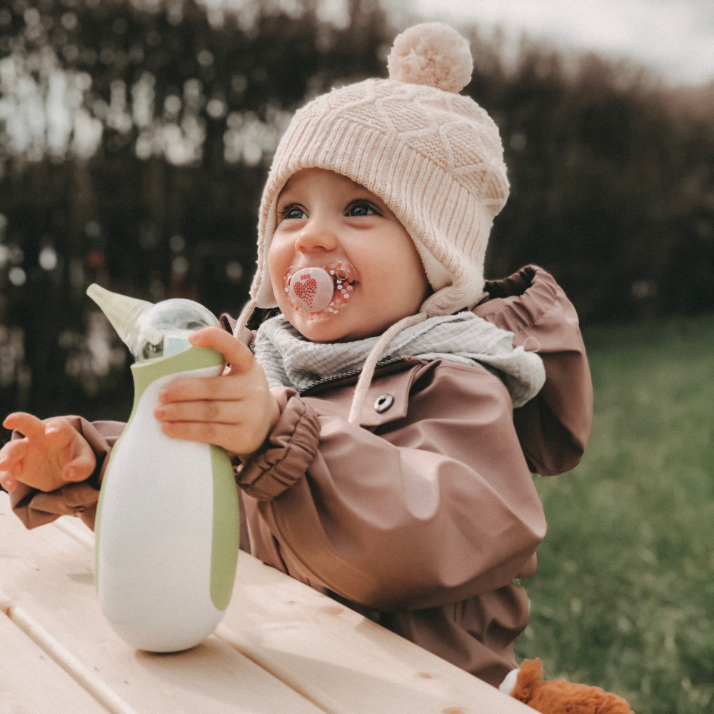 Bambina all'aperto in abiti caldi con un aspiratore nasale portatile ed elettrico Nosiboo Go in mano