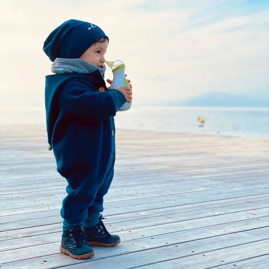 Ragazzino vicino al lungomare in inverno, con un aspiratore nasale elettrico portatile Nosiboo Go in mano