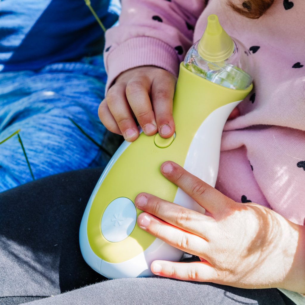 Bambina con un aspiratore nasale elettrico portatile Nosiboo Go in mano
