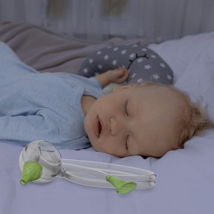 A baby boy sleeping peacefully in his bed next to the Nosiboo Eco Manual Nasal Aspirator