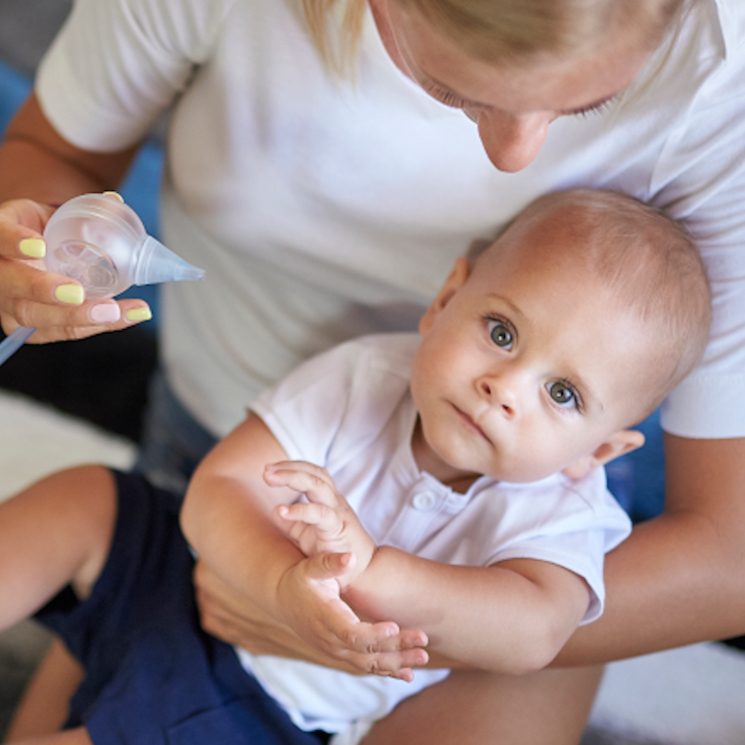 Un bambino carino tra le braccia della sua mamma che pulisce il naso del bambino con l'aspiratore nasale elettrico Nosiboo Pro